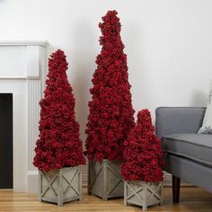 three red christmas trees sitting next to each other on top of a wooden floor in front of a fireplace