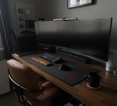 a computer desk with a keyboard, mouse and coffee cup on it in front of a large flat screen tv