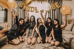 four women sitting on the floor holding up balloons and posing for a photo with their arms in the air