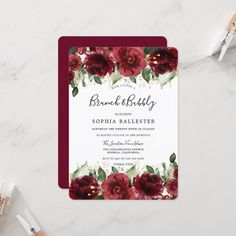 the burgundy floral wedding stationery is displayed on a marble table with flowers and greenery