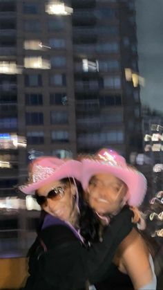 two women wearing pink hats in front of a cityscape with buildings and lights