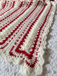 a red and white crocheted blanket laying on top of a bed