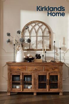 a wooden table topped with plates and vase filled with flowers next to a mirror on the wall