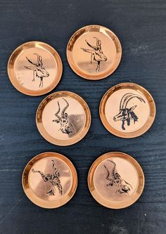 four gold plates with deer and antelope designs on them sitting on a table