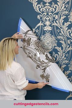 a woman is painting a wall with blue and white damask on the wall behind her