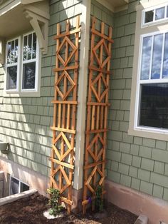 a wooden trellis on the side of a house next to a flower bed and window