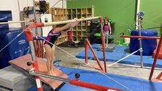 a woman is practicing on the parallel bars in a gymnastics studio with other equipment behind her