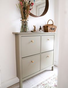 a white dresser with flowers in a vase and a mirror on the wall above it