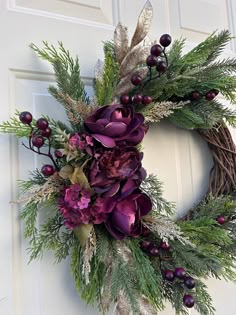 a wreath with purple flowers and greenery hanging on a door