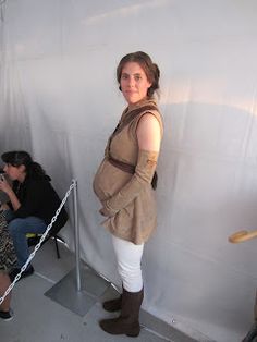 a woman dressed as star wars character standing in front of a white wall with people sitting around