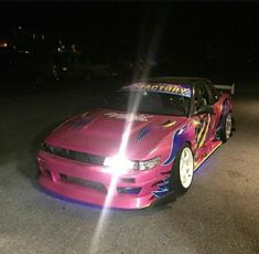 the car is painted pink and blue with flames on it's hood, parked in a parking lot at night