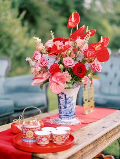 a vase filled with red flowers sitting on top of a table next to tea cups