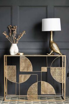 a gold console table with a white lamp and vase on the side, in front of a gray wall