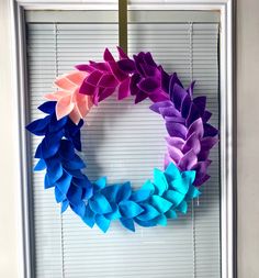 a wreath made out of colored paper sitting on top of a window sill next to blinds