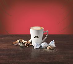 a cup of coffee sitting on top of a wooden table next to some candies