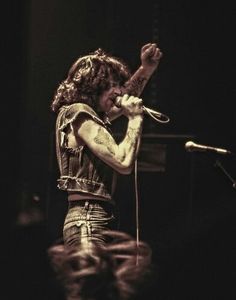 a man with long hair and tattoos on his arm holding a microphone in front of him