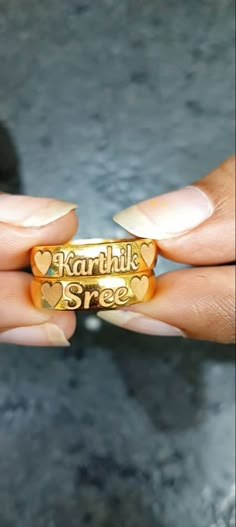 a woman's hand holding two gold rings with hearts and words engraved on them