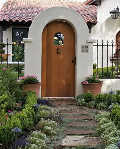 a house with a large wooden door surrounded by greenery and potted plants in front of it