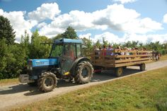 a tractor pulling a trailer filled with people on the side of a road in front of some trees