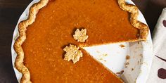 a pumpkin pie on a white plate with a piece cut out and ready to be eaten