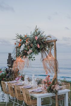 a table set up with flowers and greenery for an outdoor dinner by the ocean