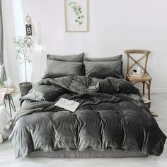 a bed with black sheets and pillows in a white room next to a chair, table and pictures on the wall