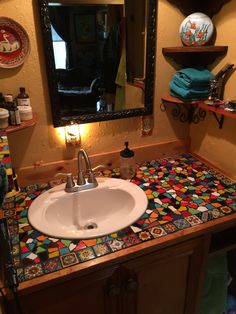 a bathroom sink sitting under a mirror next to a counter top with colorful tiles on it