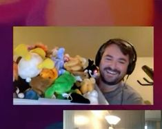 a man with headphones is smiling in front of a pile of stuffed animal toys