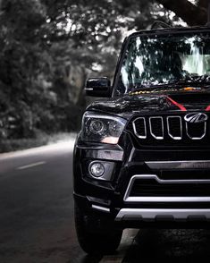 the front end of a black jeep parked on a road with trees in the background