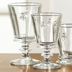 three clear glass goblets sitting on top of a wooden table next to each other