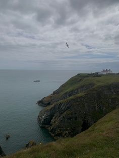 a bird flying over the ocean on a cloudy day with a boat in the distance