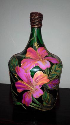 a green glass bottle with pink flowers painted on the side and brown wire wrapped around it