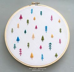 a cross stitch pattern with colorful trees on white fabric in a circle hoop hanging on a wall