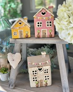 three little houses are sitting on top of a wooden shelf with flowers in the background