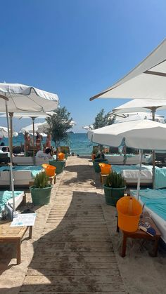 an outdoor swimming area with tables and umbrellas on the beach, along with people lounging in lounge chairs