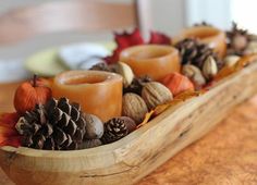 a wooden tray filled with candles and pine cones