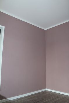 an empty room with pink walls and wood flooring is seen in this image from the corner