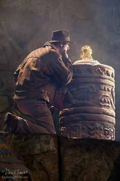 a man in a hat and coat is leaning on a large object