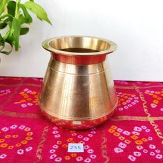 a gold vase sitting on top of a pink table cloth next to a potted plant