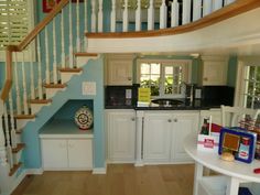 a kitchen with blue walls, white cabinets and wooden stairs leading up to the second floor