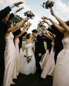 a bride and groom are surrounded by their bridal party guests holding flowers in the air