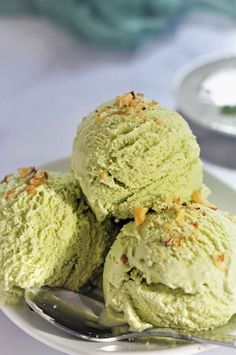 three scoops of green tea ice cream on a white plate with a silver spoon