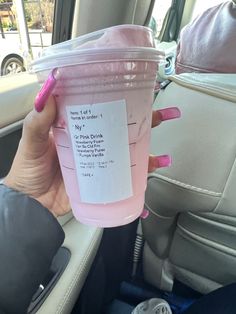 a woman holding up a pink drink in her car