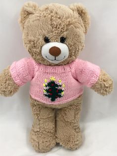 a teddy bear wearing a pink sweater with a christmas tree on it's chest