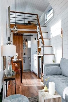 a living room filled with furniture next to a wooden floor and white walls, along with a staircase leading up to the upper level