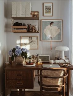 a wooden desk topped with a laptop computer next to a lamp and pictures on the wall