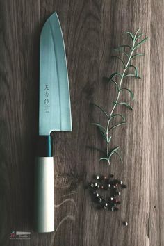 a knife sitting on top of a wooden table next to some berries and an olive branch