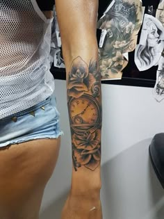 a woman's arm with a clock tattoo on it and flowers in the background