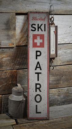 an old ski patrol sign hanging on the side of a wooden wall next to a watering can