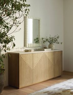 a wooden dresser sitting next to a mirror and potted plant on top of a hard wood floor